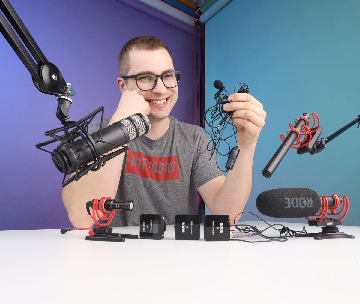 Bartek Dziedzic przy biurku z kilkoma mikrofonami: podcastowym na ramieniu, krawatowymi i kierunkowym